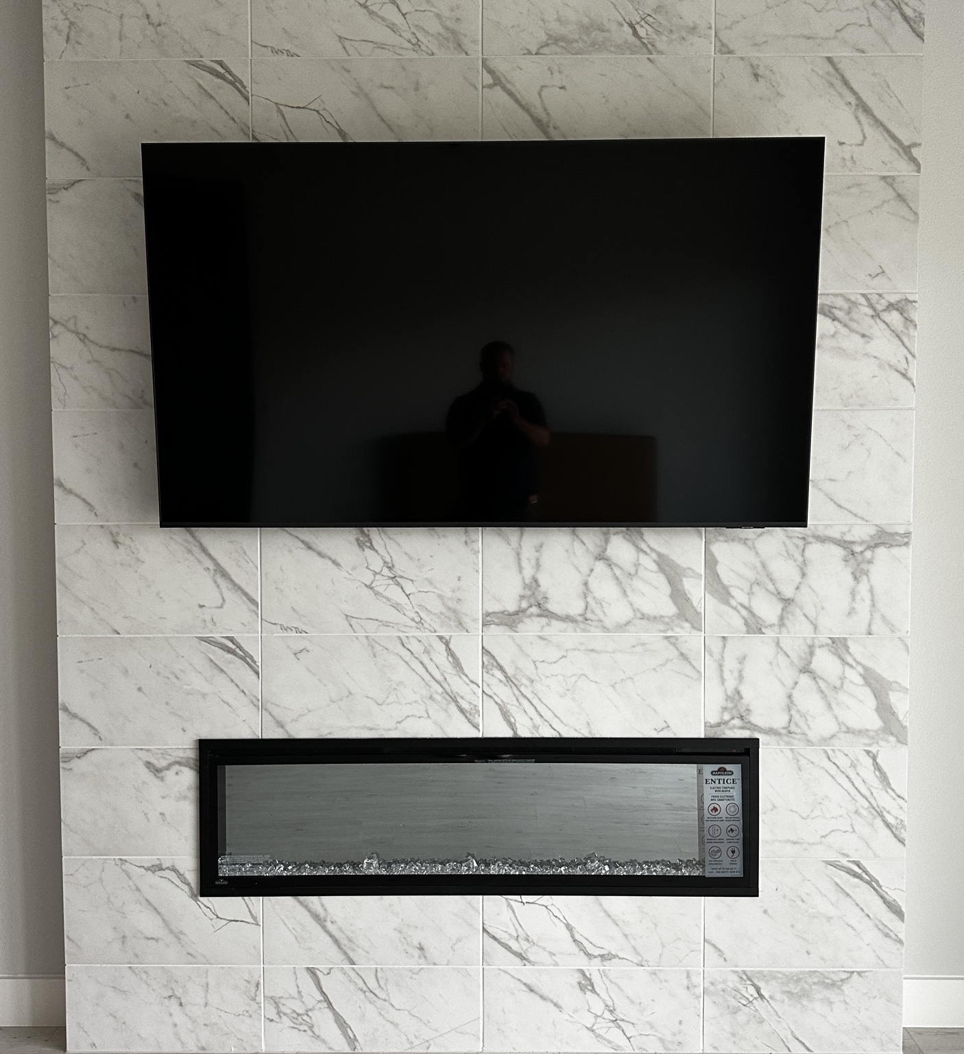 Large TV mounted above an electric fireplace on a marble-tile feature wall